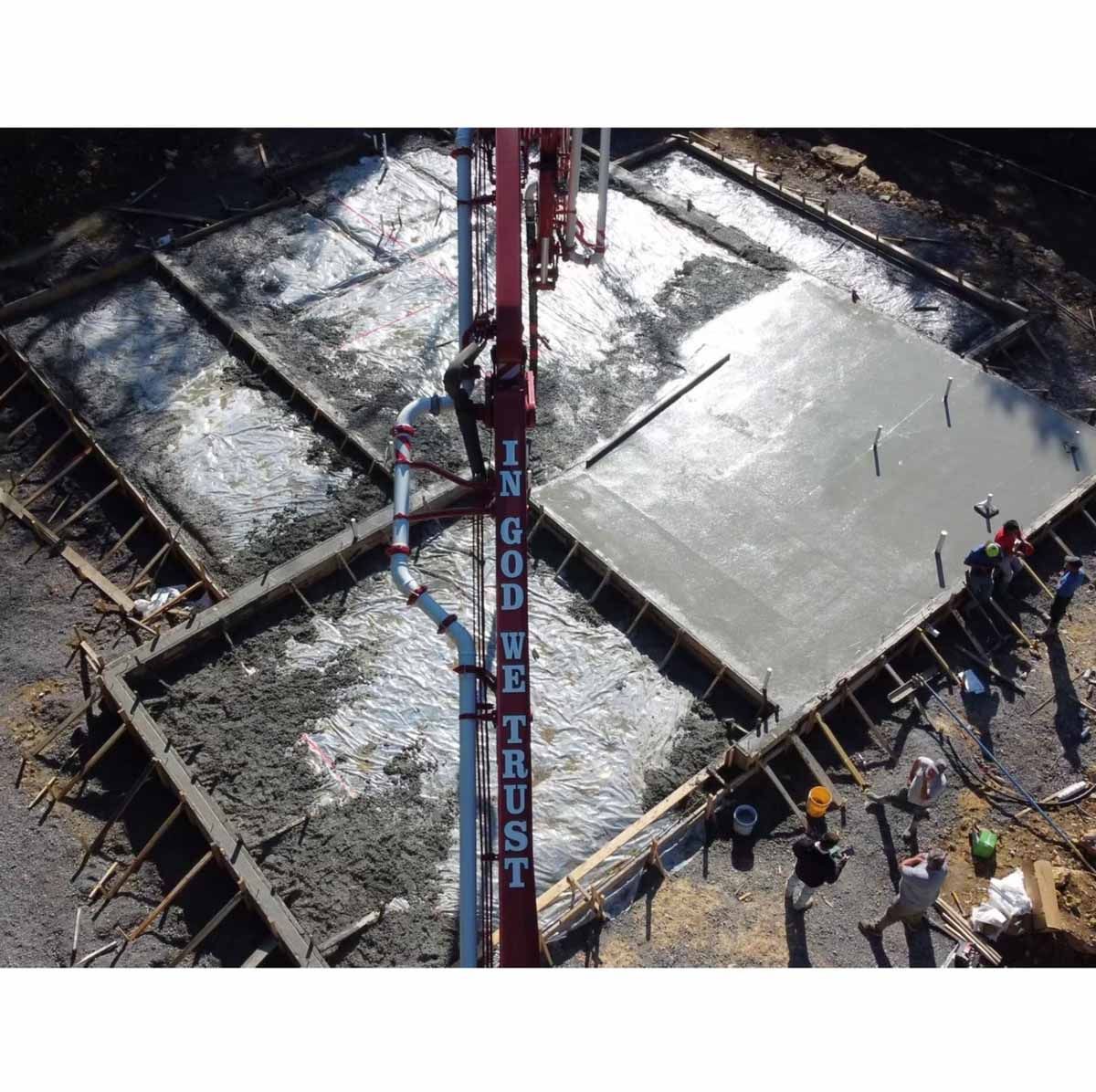 Construction site with concrete being poured into forms from a red pump truck, workers present.