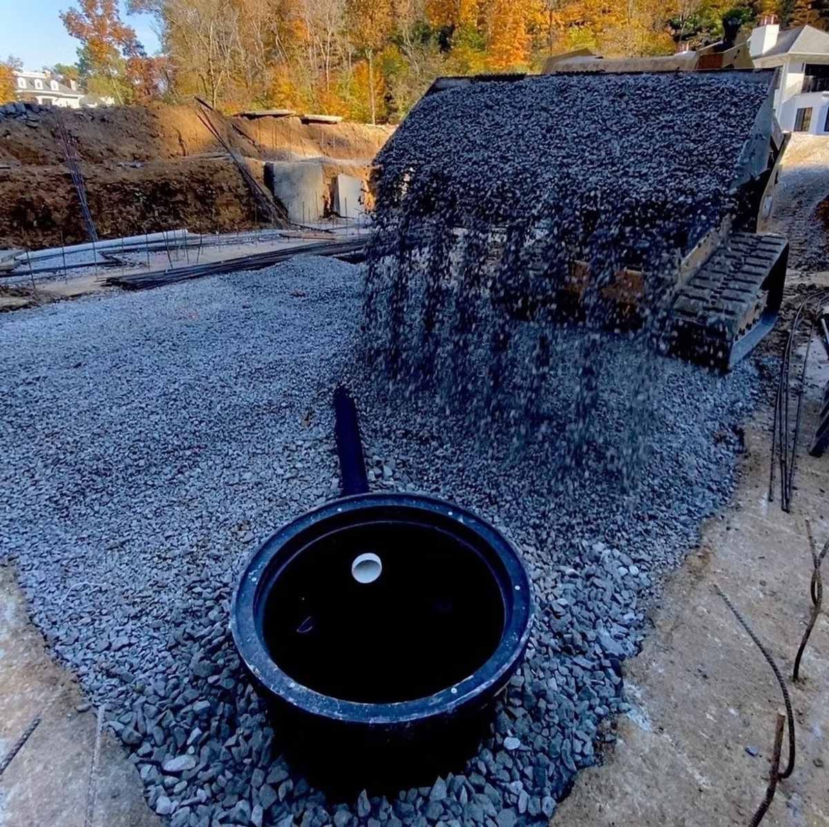 Construction site with a gravel base, a small building covered in black material, and a black water basin.