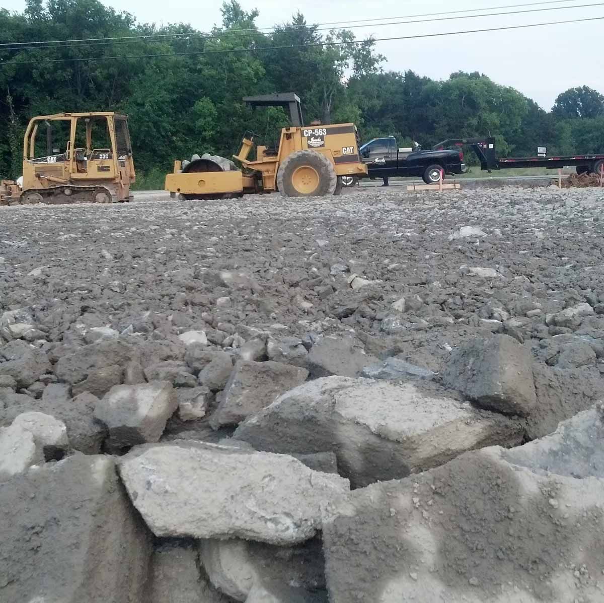 Construction site: Yellow bulldozers on rocky ground, trees in background.