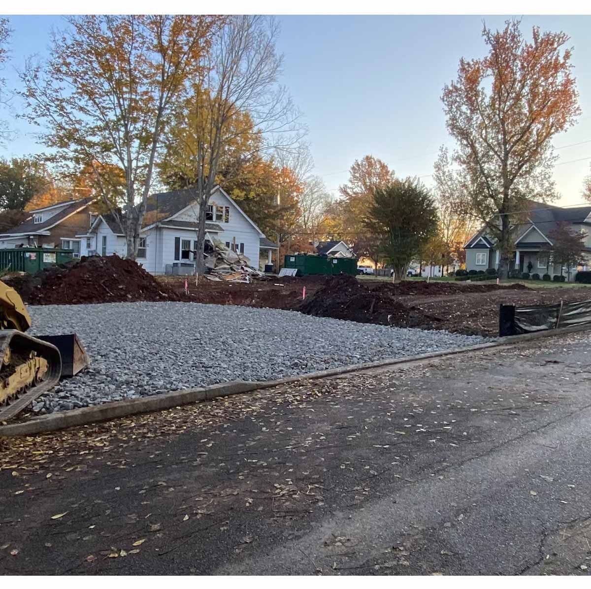 Construction site: gravel and dirt piles in front of houses; autumn trees and gray sky.