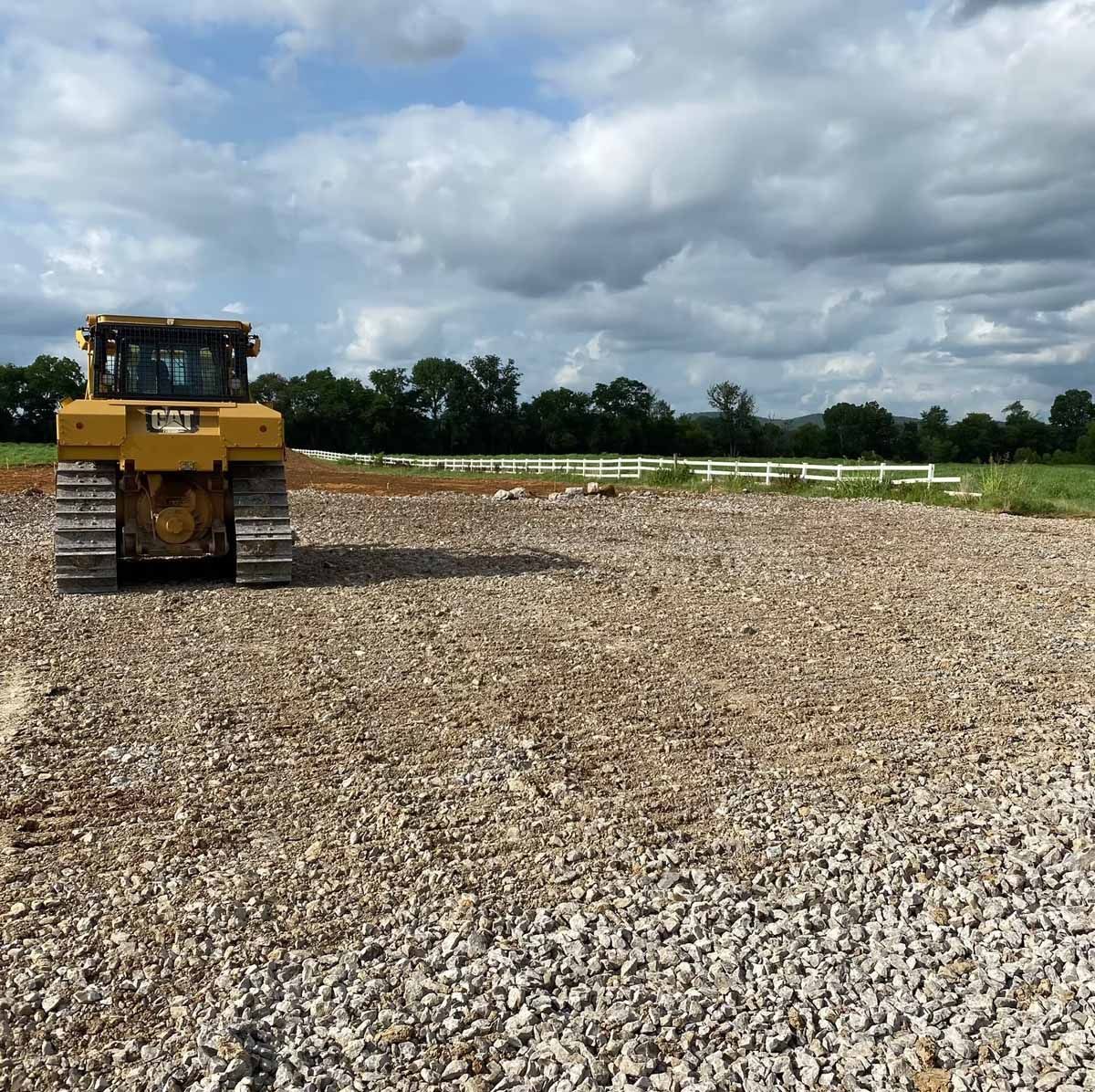 Yellow bulldozer on gravel, preparing a field under a cloudy sky.