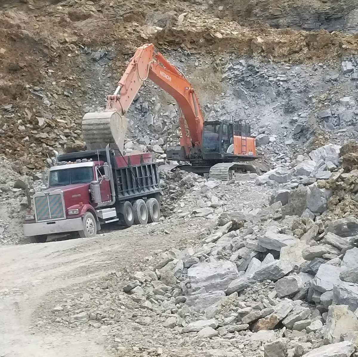An excavator loading a red dump truck with rock in a quarry.
