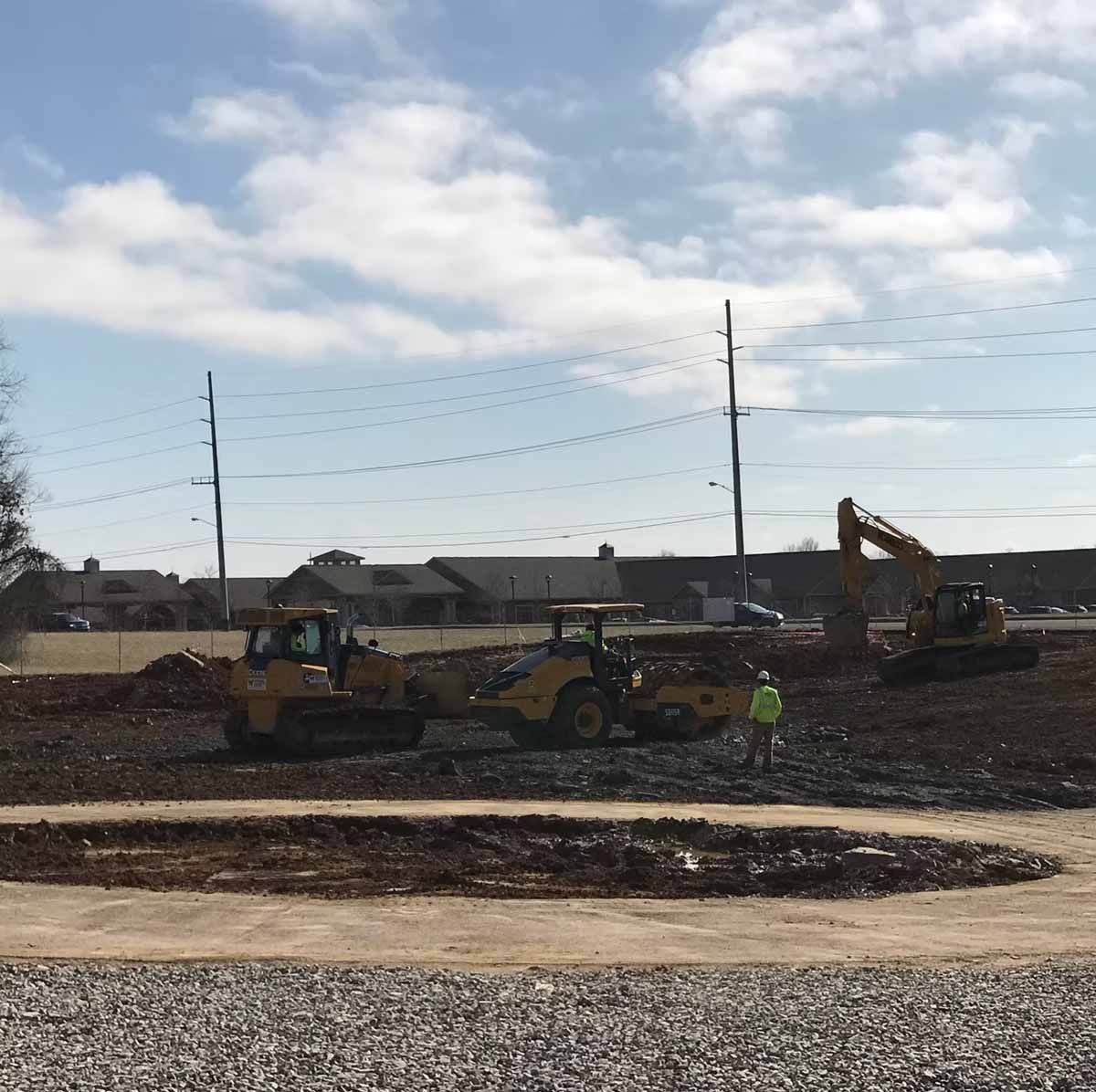Construction site with bulldozers, an excavator, and a worker operating heavy machinery on dirt. Cloudy sky.