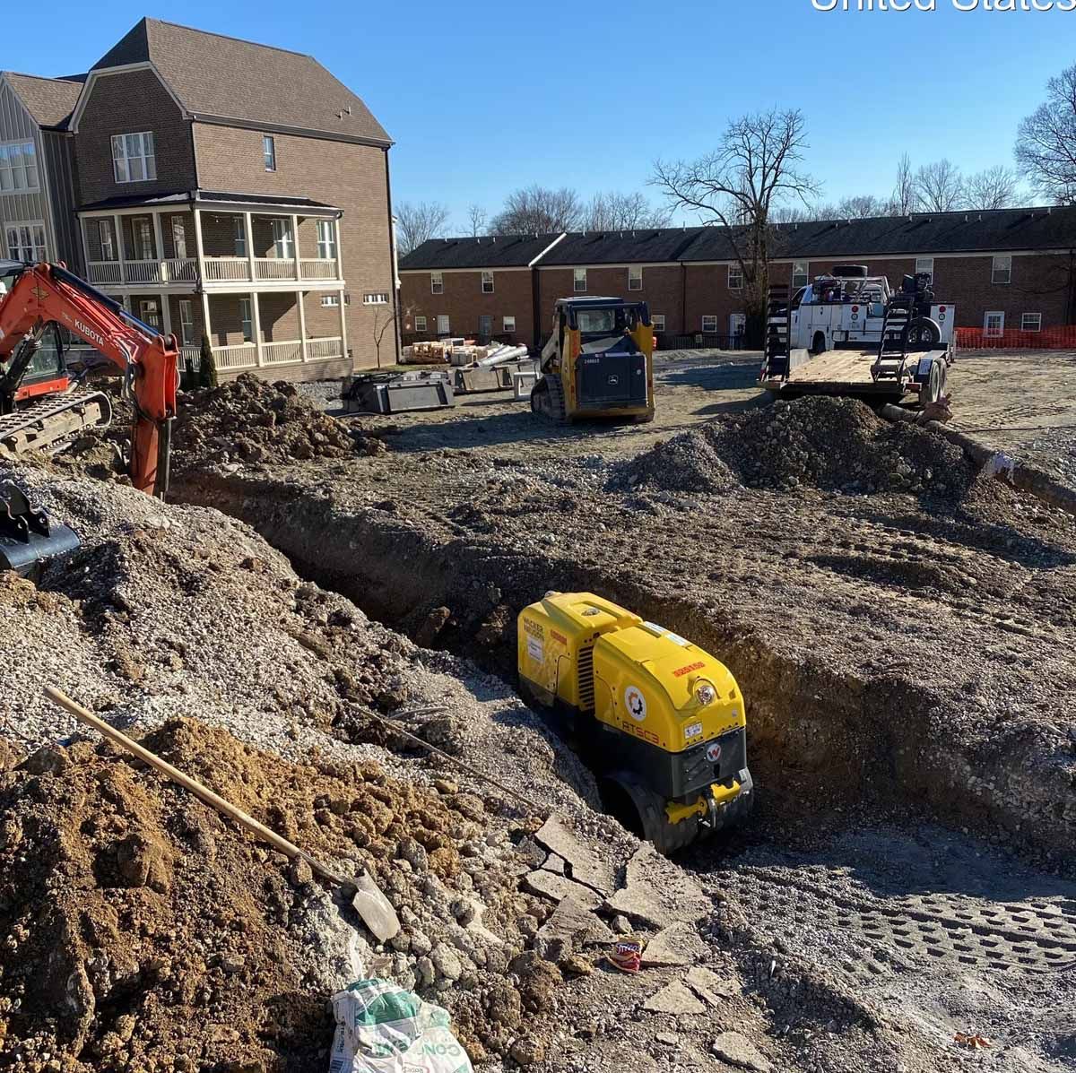 Construction site with heavy machinery digging a trench. Buildings in the background.