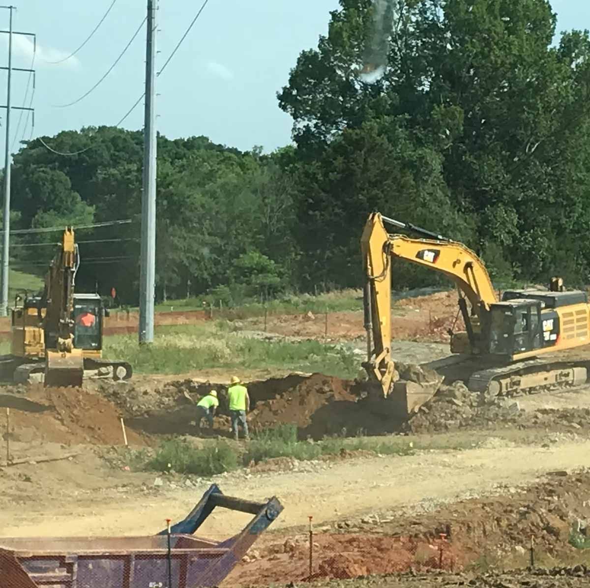 Construction site with yellow excavators, workers in vests, and earth moving.