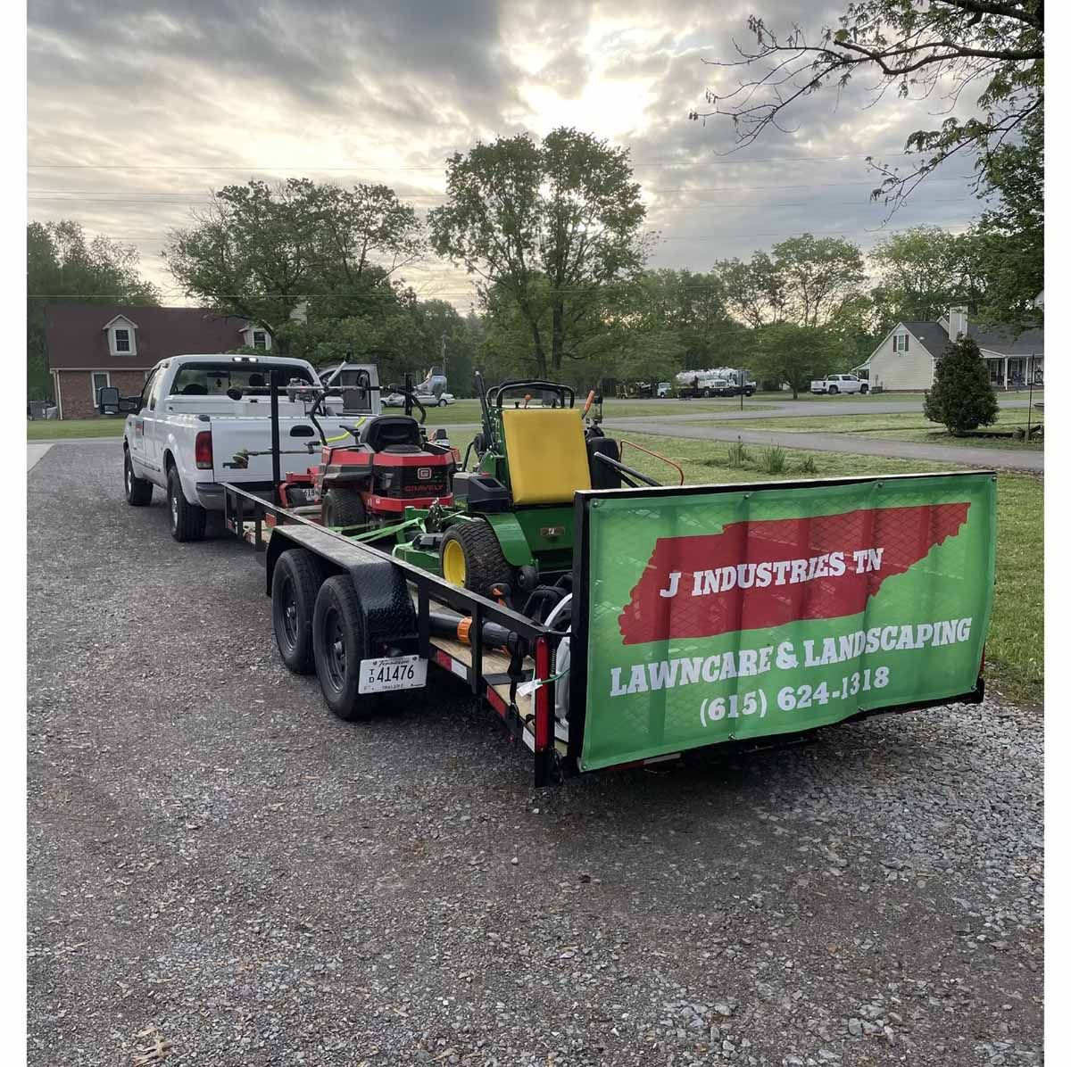 A white truck towing a trailer with lawn care equipment. Sign for 