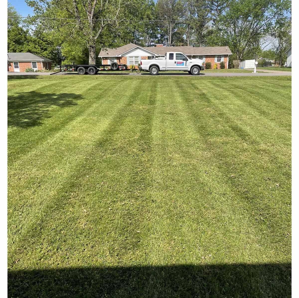 Green lawn with mowing stripes, white truck, and houses in the background.
