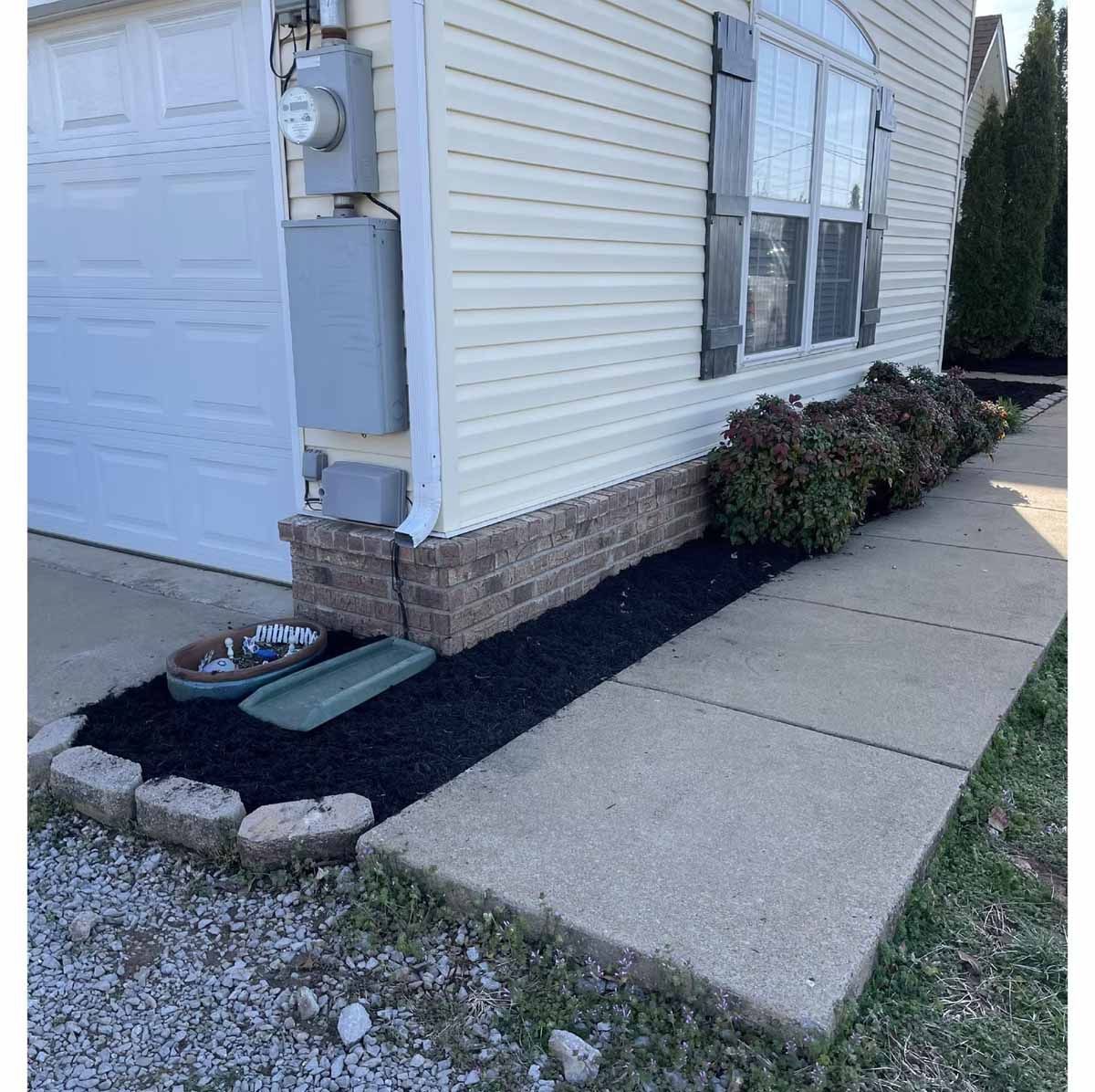 A house with a walkway and garden bed filled with black mulch.