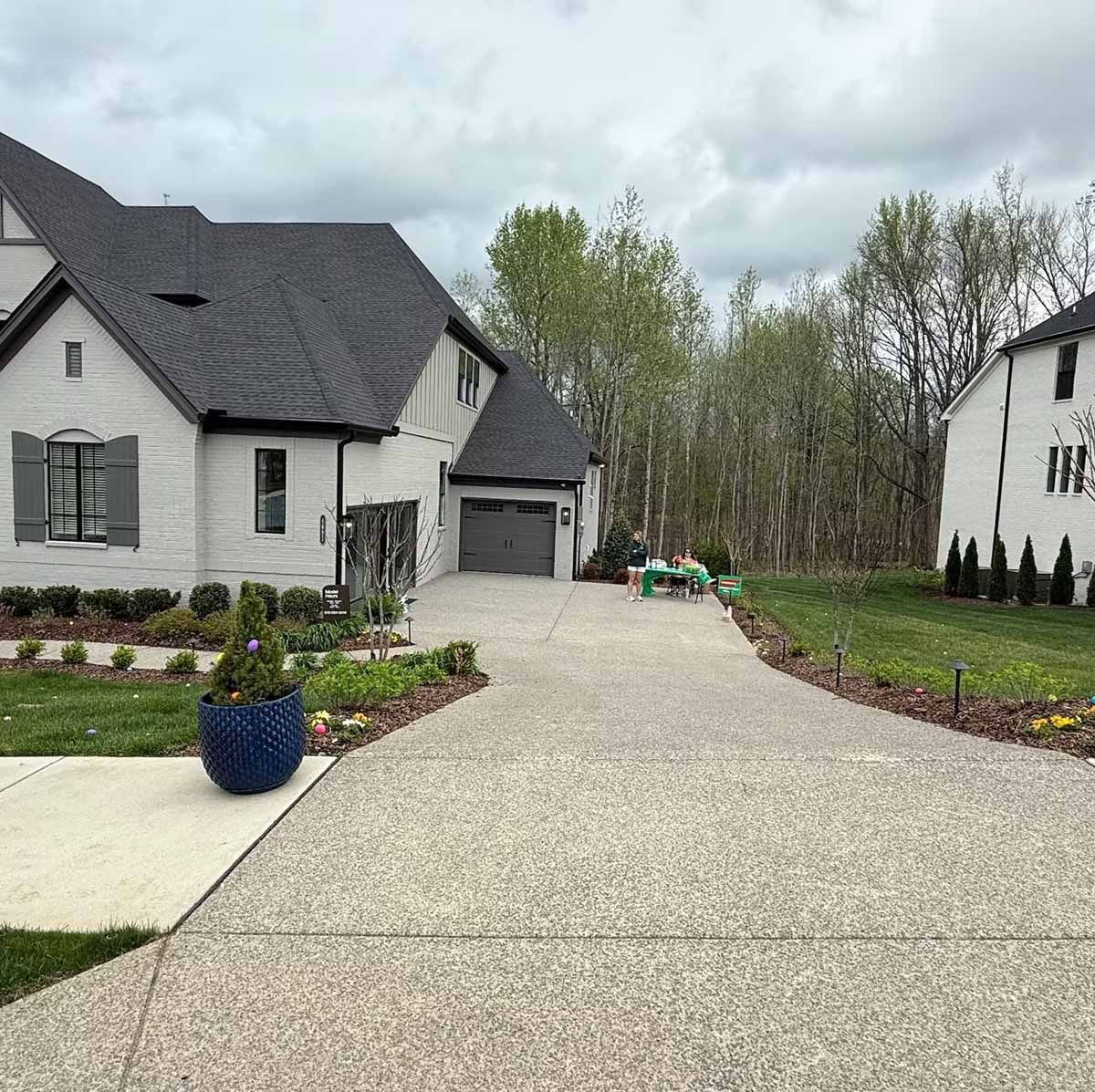 A large, light-colored brick house with a long driveway, cloudy sky.