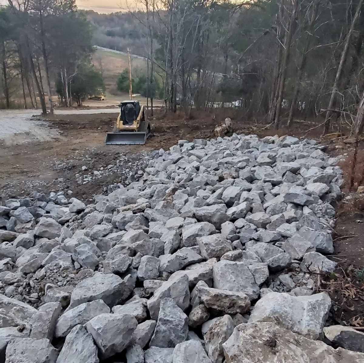 A rocky embankment in a wooded area with a small bulldozer.