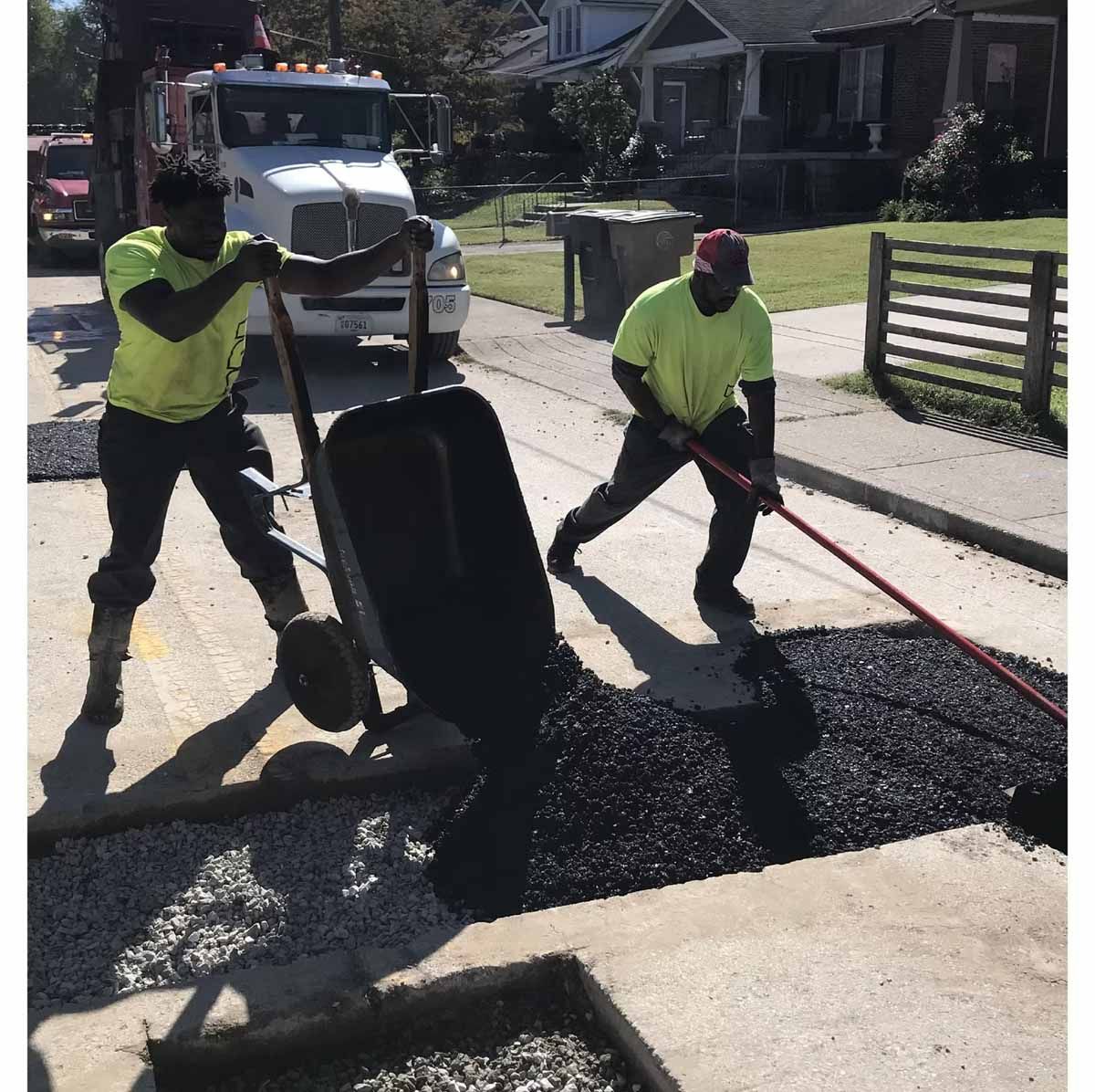 Two workers in neon shirts paving a street with asphalt.