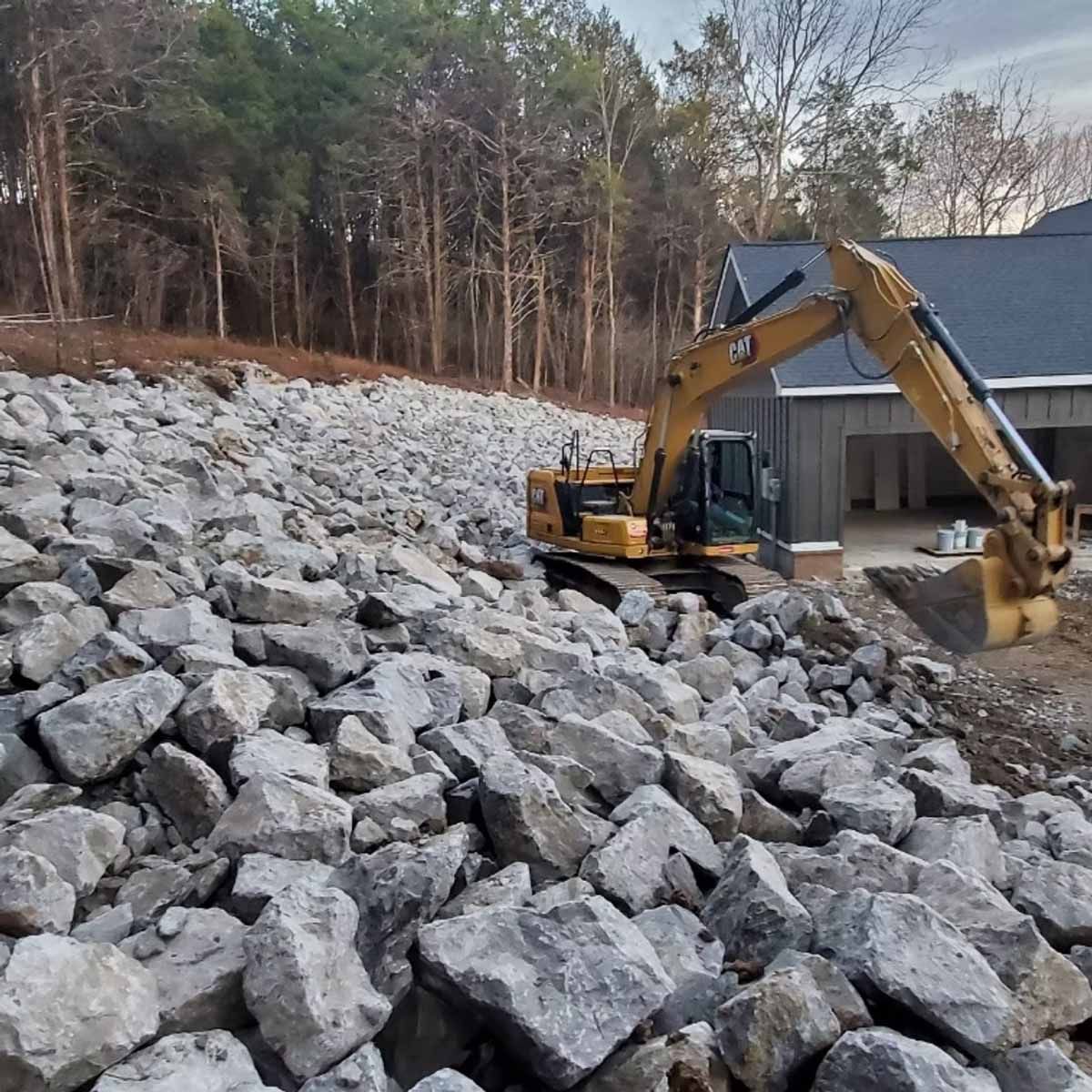 Yellow excavator placing rocks on a hillside next to a house.