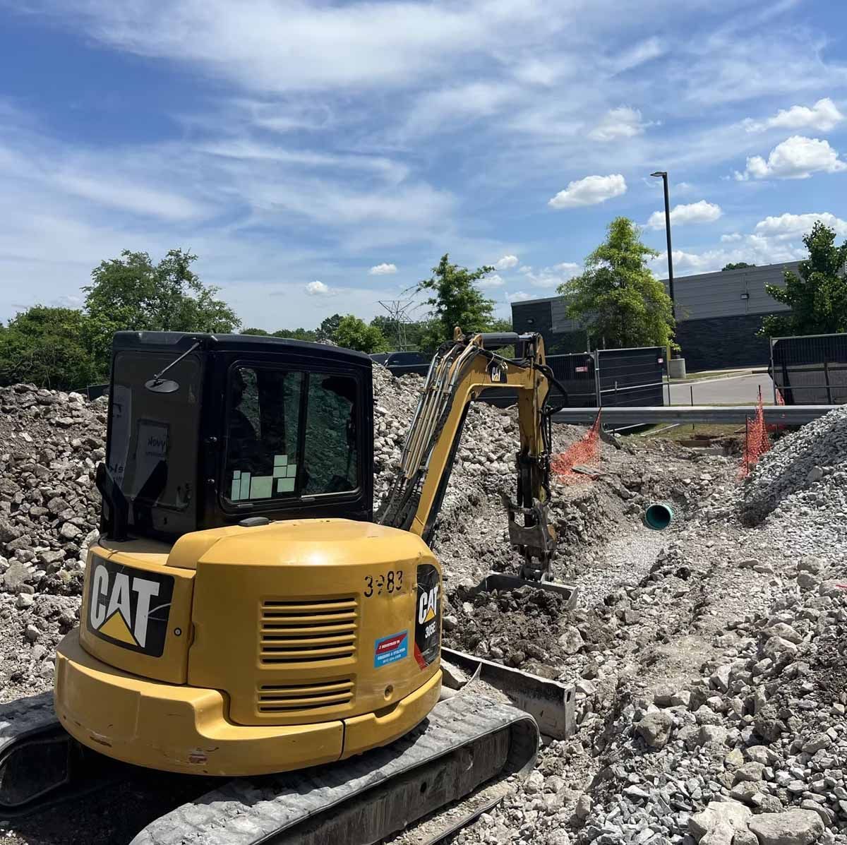Yellow CAT excavator digging in dirt, construction site, blue sky.