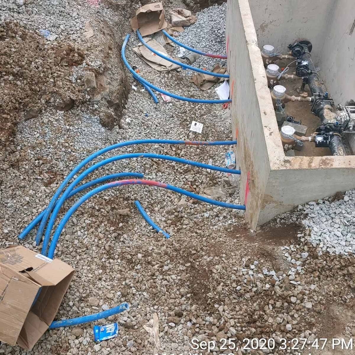Blue pipes connected to valves in a concrete box, amidst gravel.