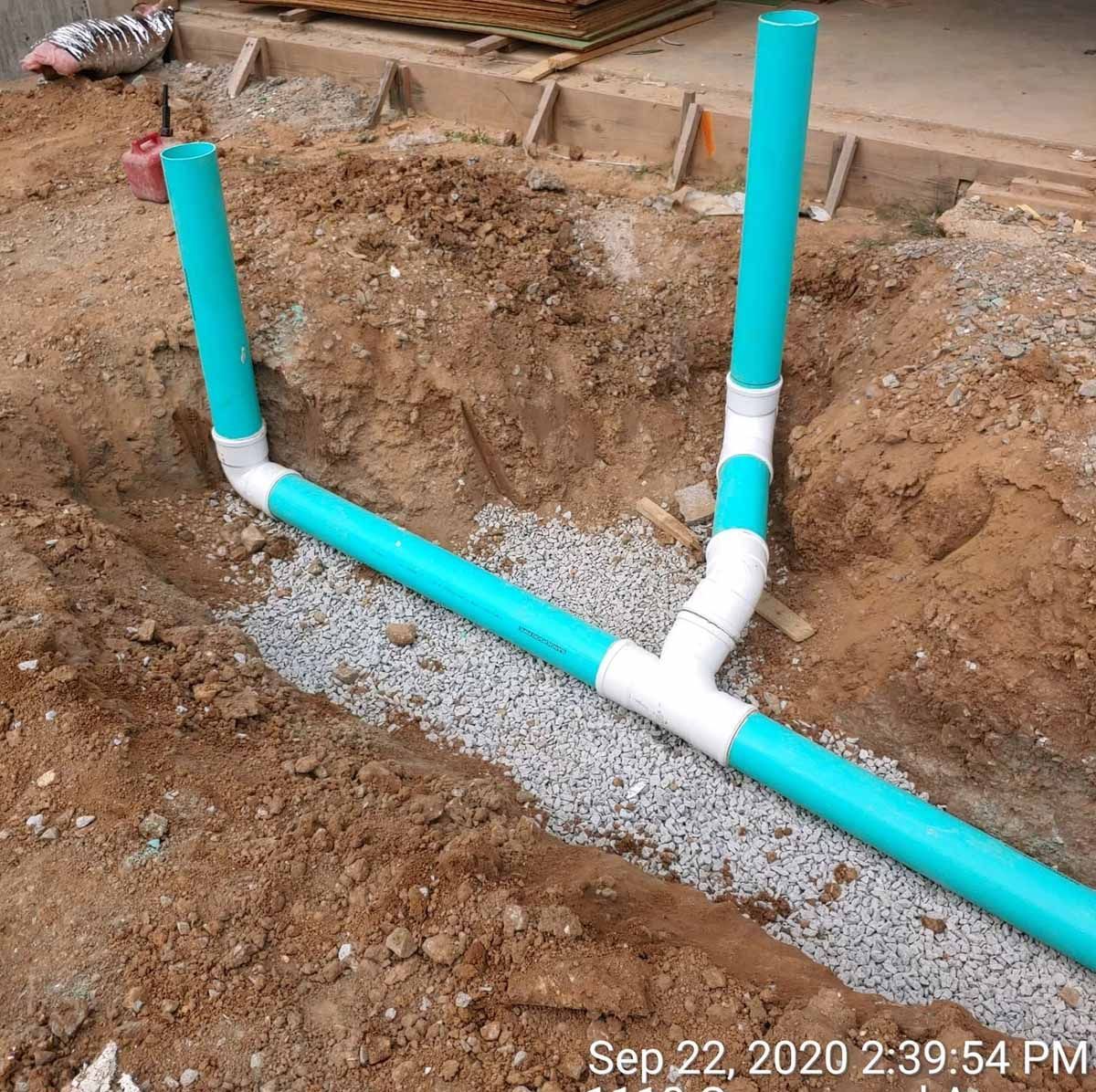 Blue PVC plumbing pipes in a trench, connected with white fittings, on a construction site.