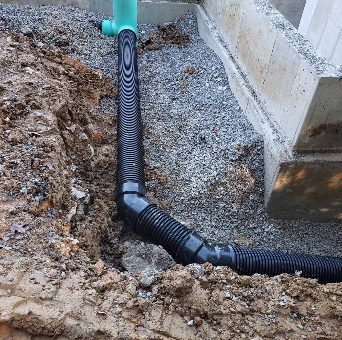 Black corrugated drainage pipe installed next to a concrete foundation.