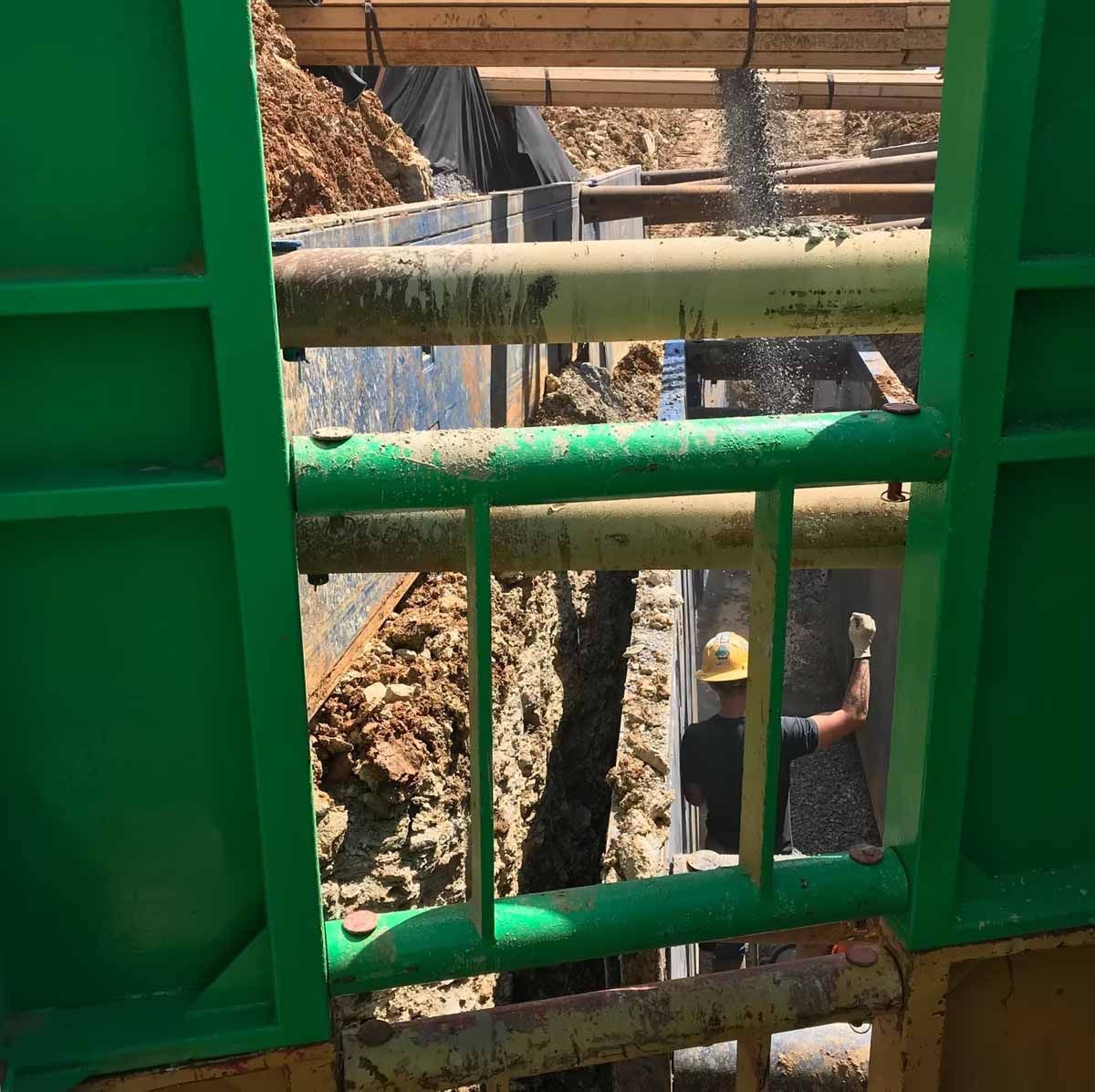 Green trench box protects a construction worker in a deep excavation.