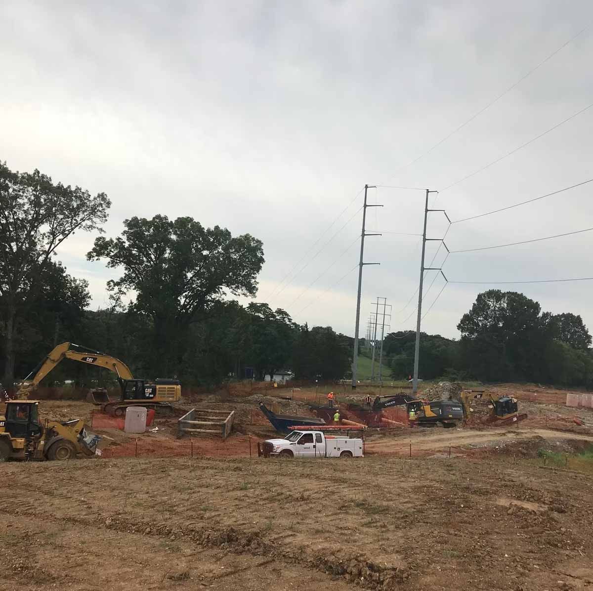 Construction site with heavy machinery, power lines, and a cloudy sky.