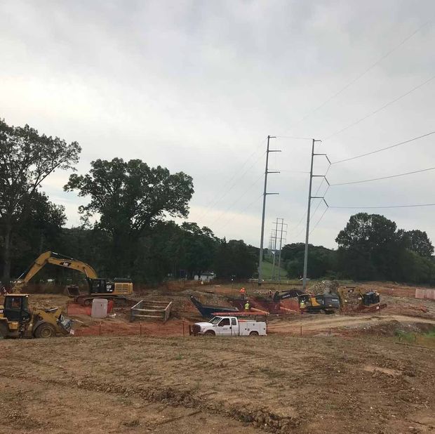 Construction site with heavy machinery, power lines in background, cloudy sky.