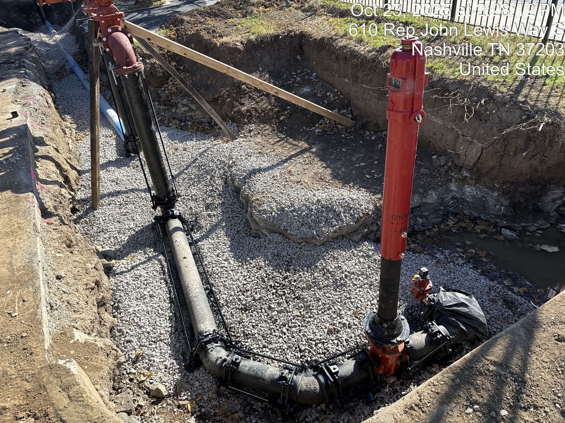 A construction trench with exposed black water pipes and a tall red fire hydrant, bedded in gravel and dirt.