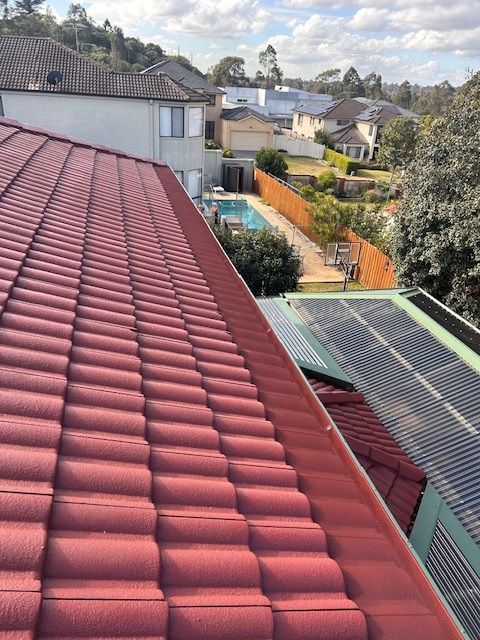 Red tiled roof with guttering in the foreground; a suburban neighborhood with a pool is visible in the background.