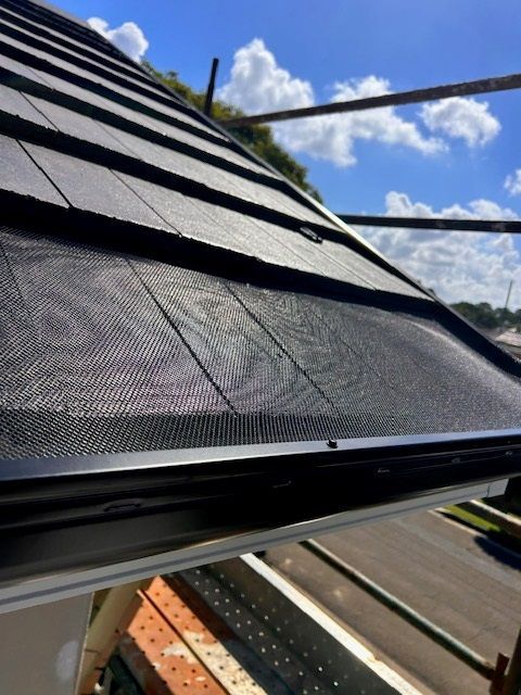 Black roof with mesh gutter guards installed, along with scaffolding and bright blue sky.