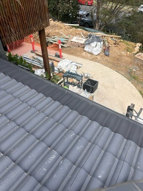 Gray tiled roof overlooking a construction site with building materials and a concrete path.