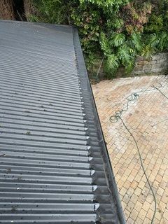 A close up of a gutter on a roof next to a brick walkway.
