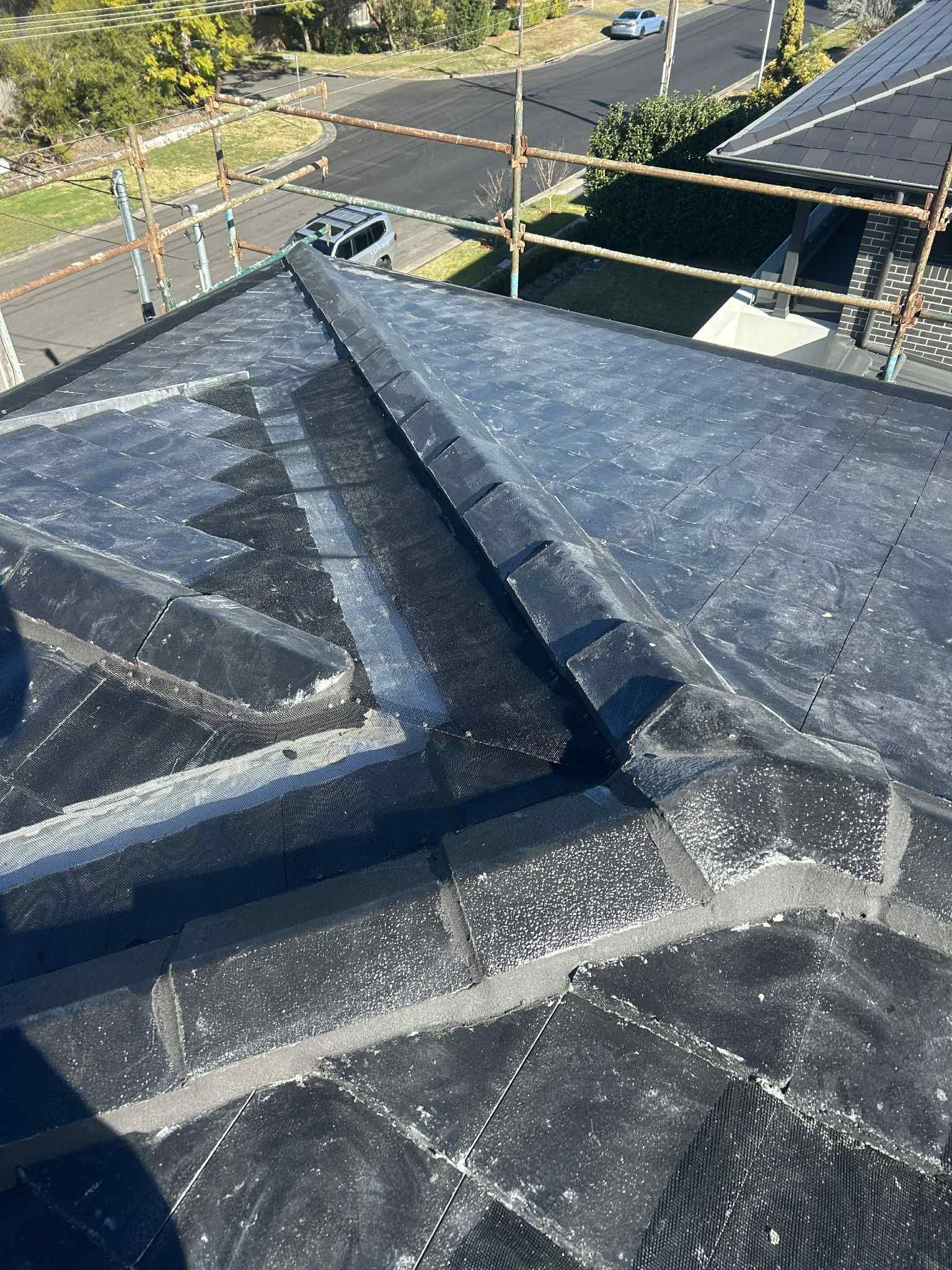 View of a black tar roof with a central ridge and flashing. Scaffolding is visible