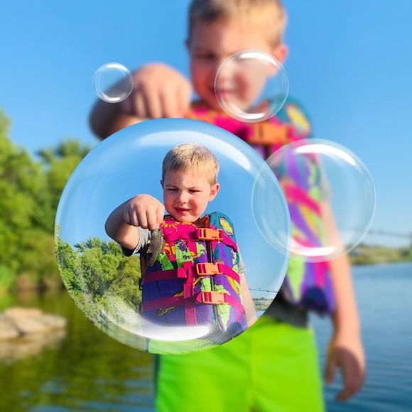 A boy is holding a soap bubble with a picture of him in it