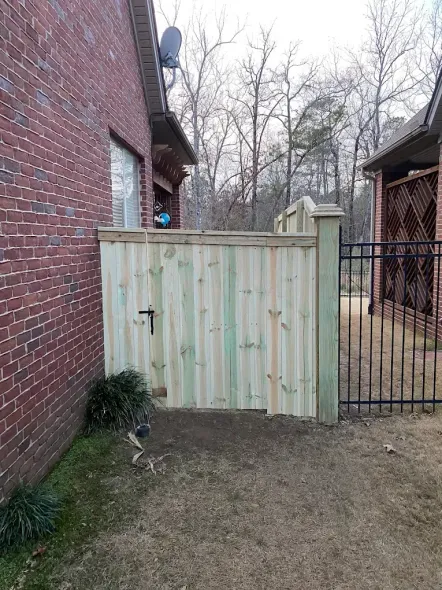 Wooden gate in front of a brick house, beside a black metal fence.