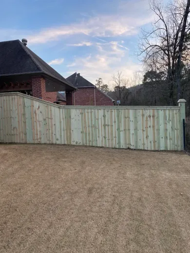 Wooden fence in a backyard, adjacent to a brick house, under a cloudy sky.