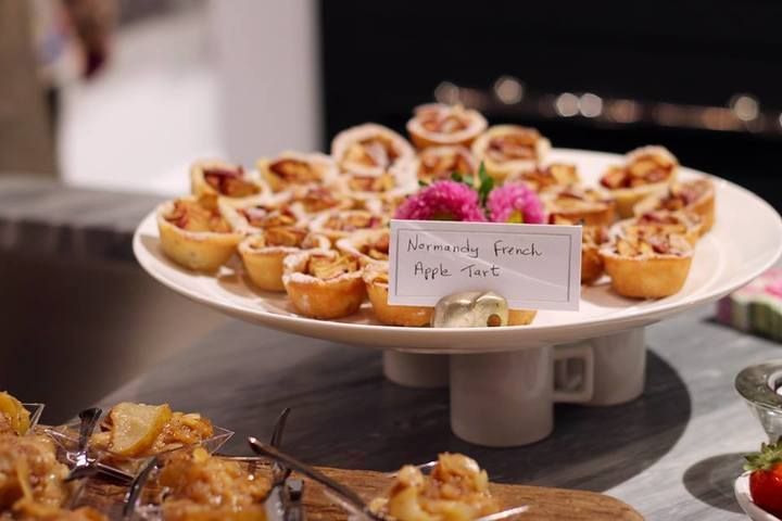 Miniature apple tarts on a white tiered serving platter. A label reads