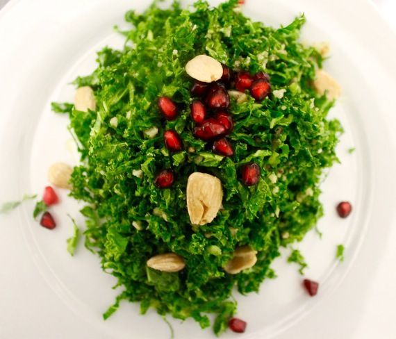Kale salad with pomegranate seeds and almonds on a white plate.