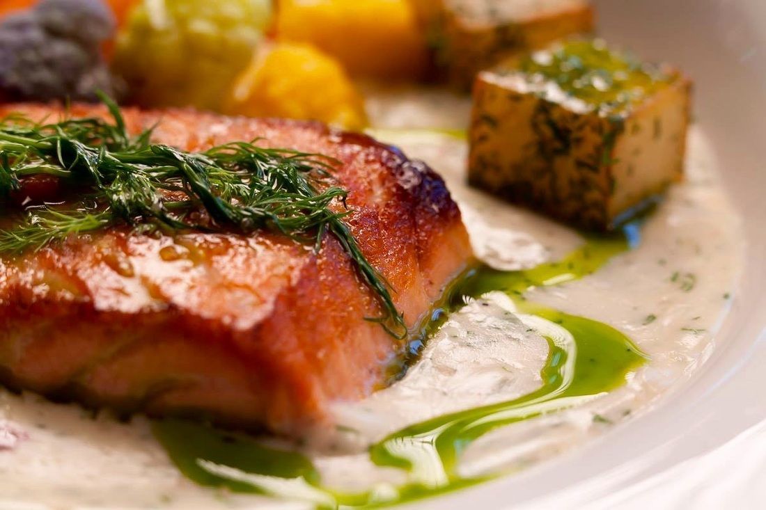 A person is holding a tong over a tray of meat.