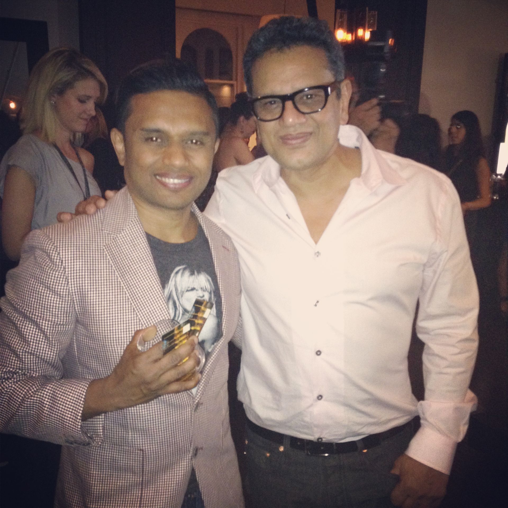 Two men smiling, arm-in-arm. One holds a small item, wearing a striped jacket.