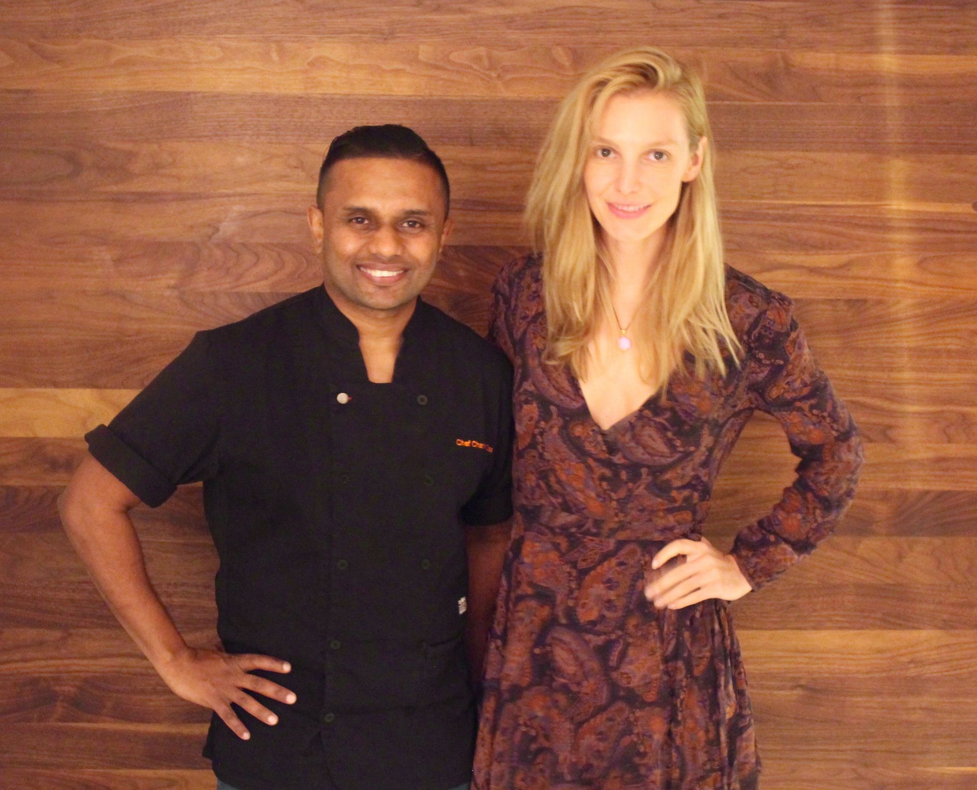 Chef and woman standing side-by-side, smiling, in front of a wood-paneled wall.
