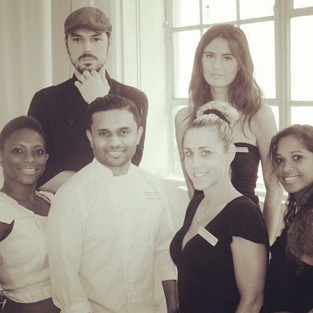 Group of six people smiling, posing together indoors with natural light, in black and white.