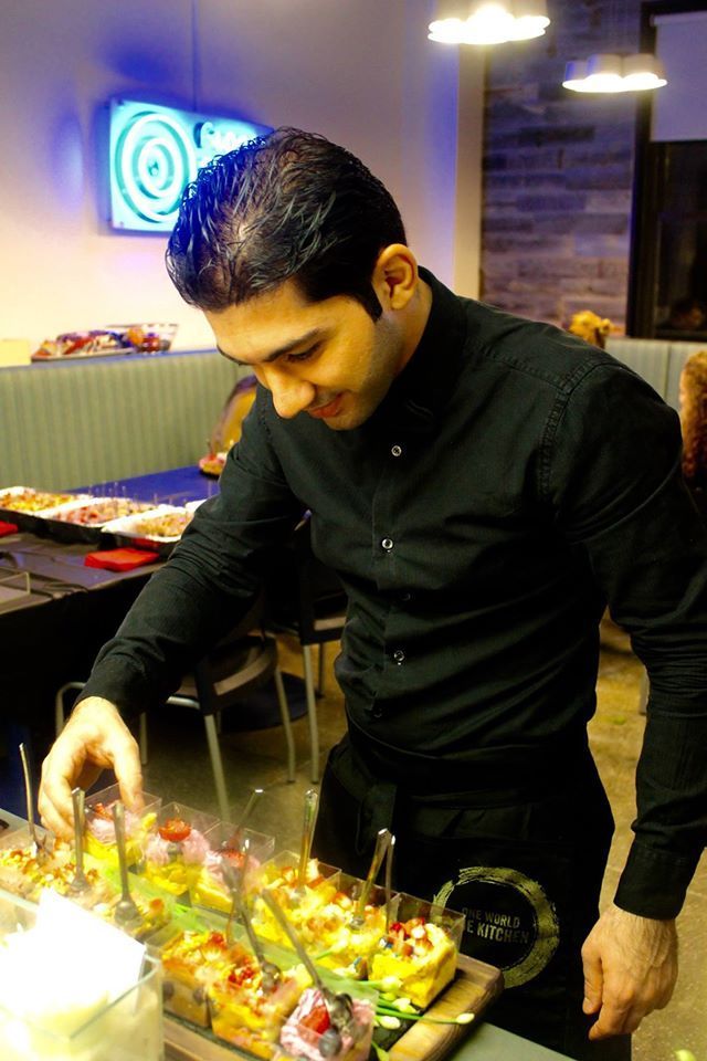 Man in black shirt arranging desserts behind a counter in a modern restaurant.