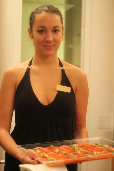 Woman holding a tray of food, wearing a black halter top and nametag, smiling. Inside.