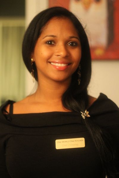 Woman with long dark hair smiles, wearing a black top with a name tag.