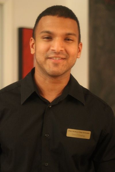 Man in black shirt smiles, wearing a name tag. Standing indoors, likely at a business.