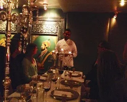 Server carrying candles at a formal dinner table, ornate chandelier, portraits on the wall.