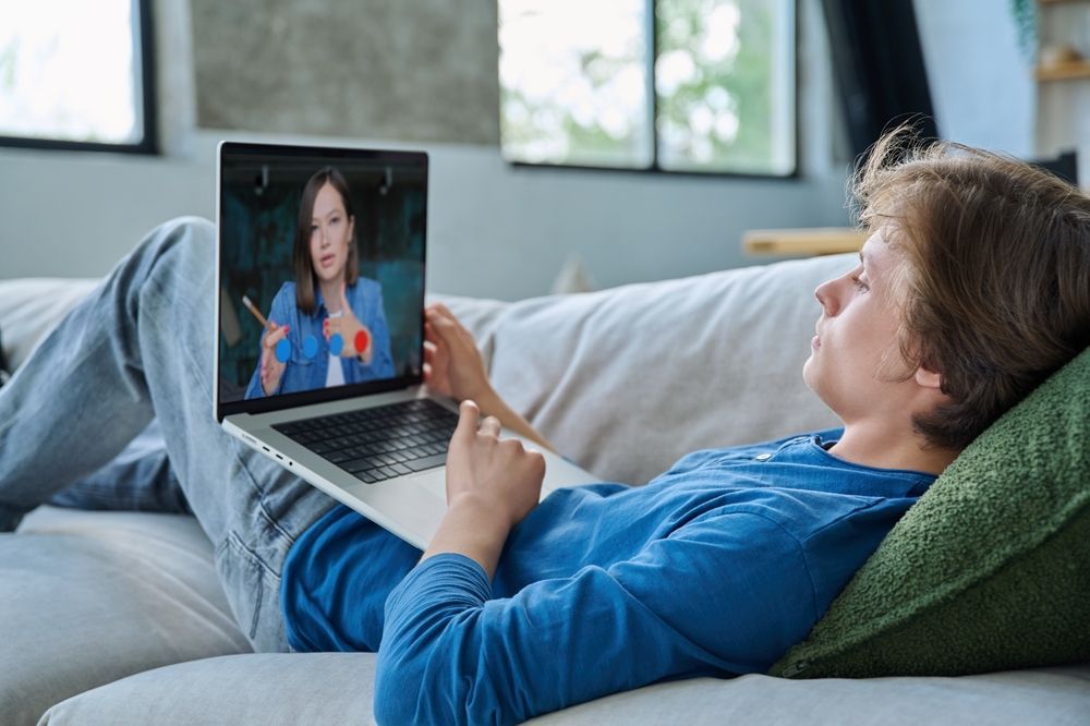 Person reclining on couch watching online lecture on laptop.