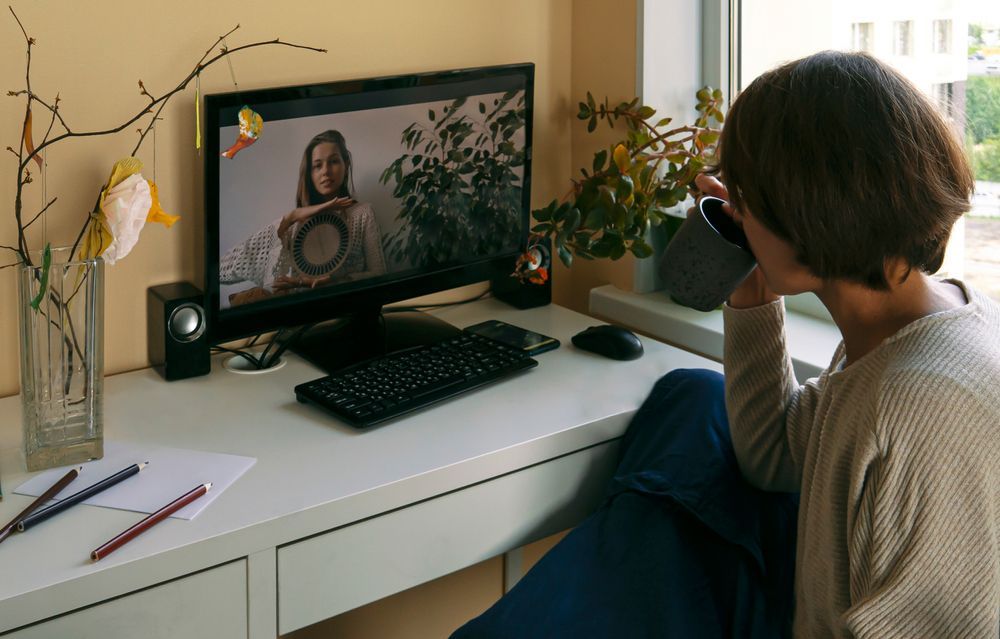 Person on a video call at a desk, looking at a computer screen.