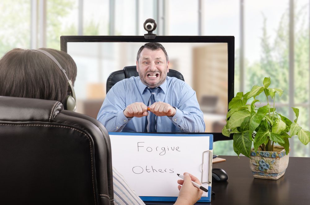 Person in chair facing computer screen. Man on screen makes angry face. Sign: