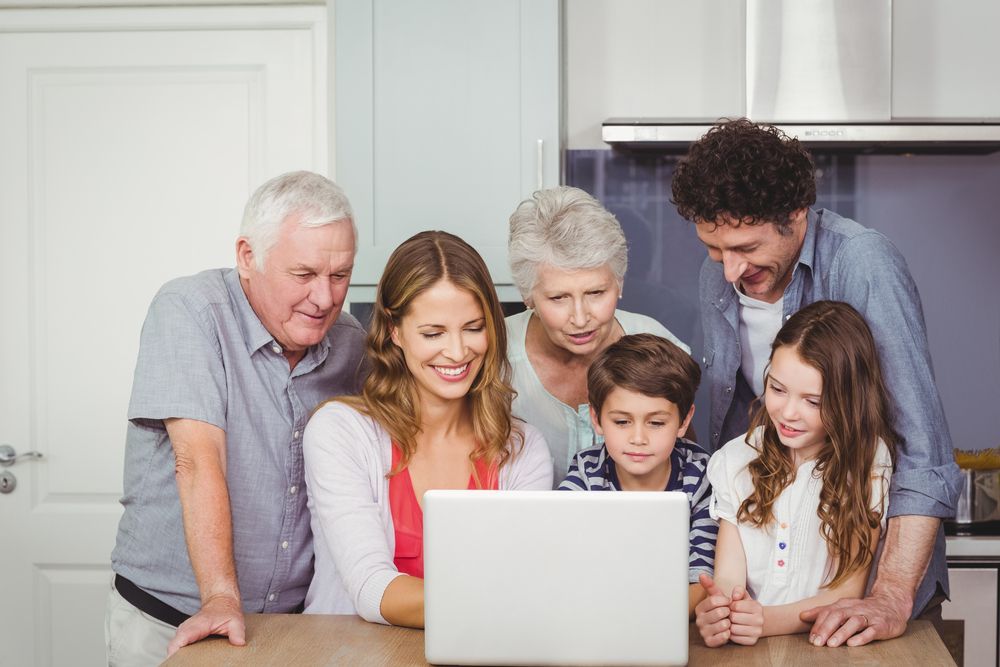 Family looking at a laptop in a kitchen, smiling.