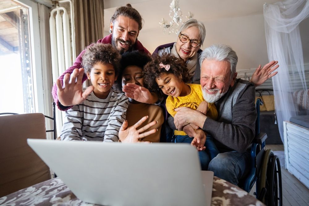 Family video call: People wave at a laptop screen in a living room.