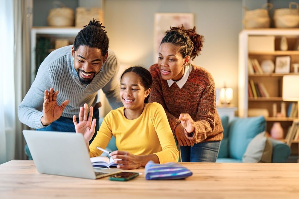 Family waves at laptop during a video call in a living room.