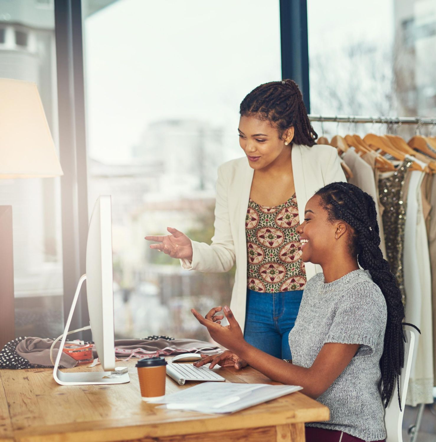 Person writing in a notebook at a table with a laptop and another person using a phone.